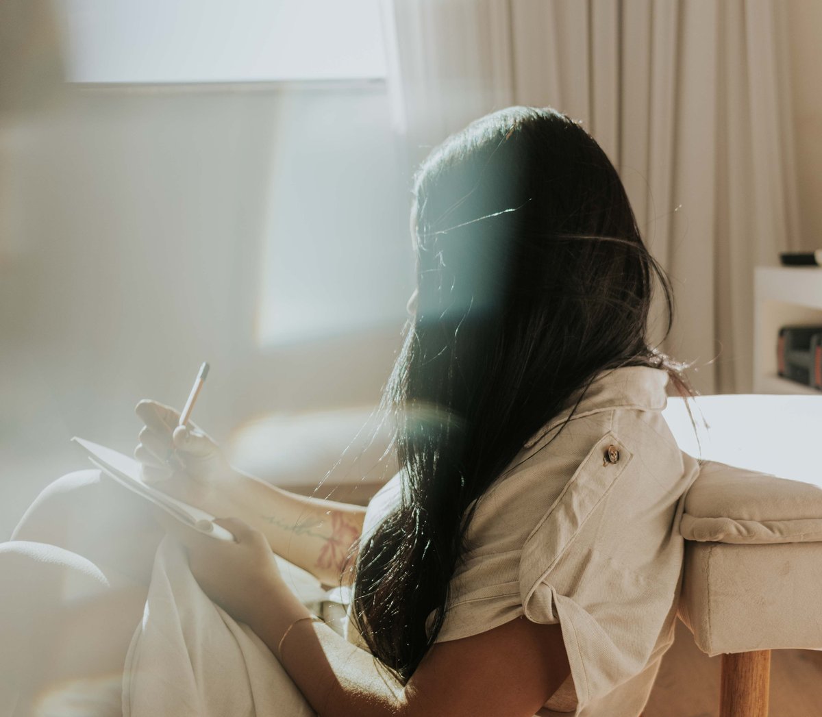 Young woman sitting and writing in a notebook, bright atmosphere of an NDG rental apartment.