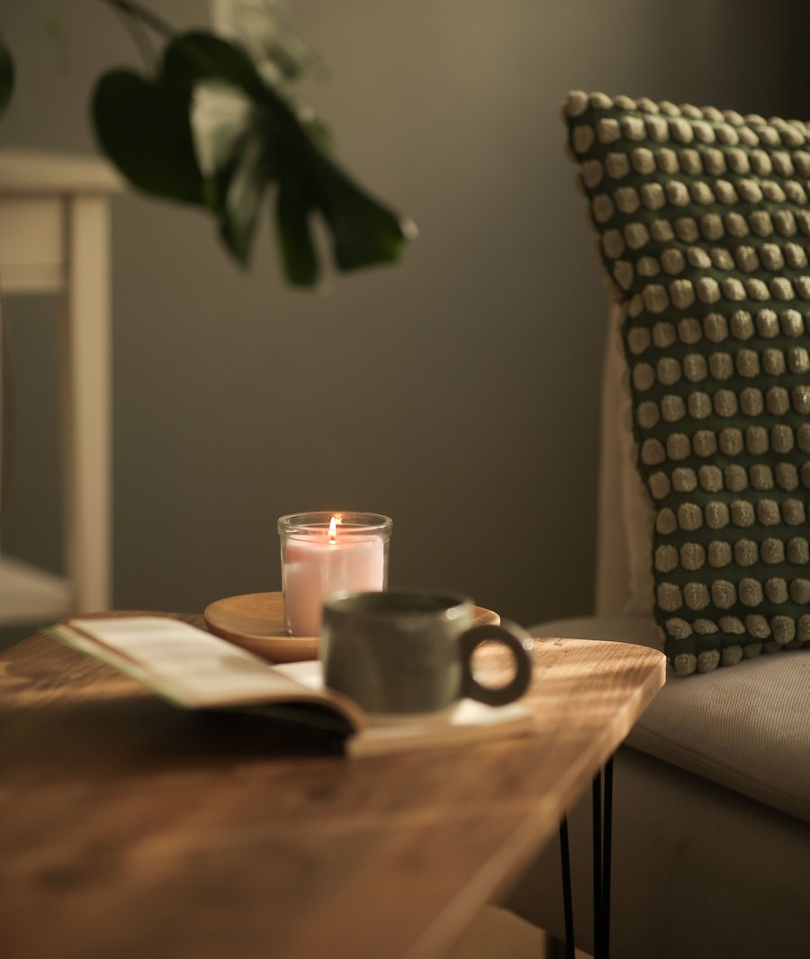 Armchair, lit candle and mug on a wooden table, reading nook of a rental home.