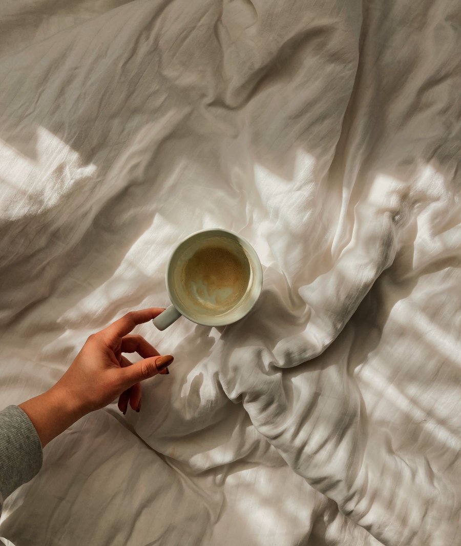 Coffee cup held over white sheets in morning sunlight, warm atmosphere of an NDG apartment.