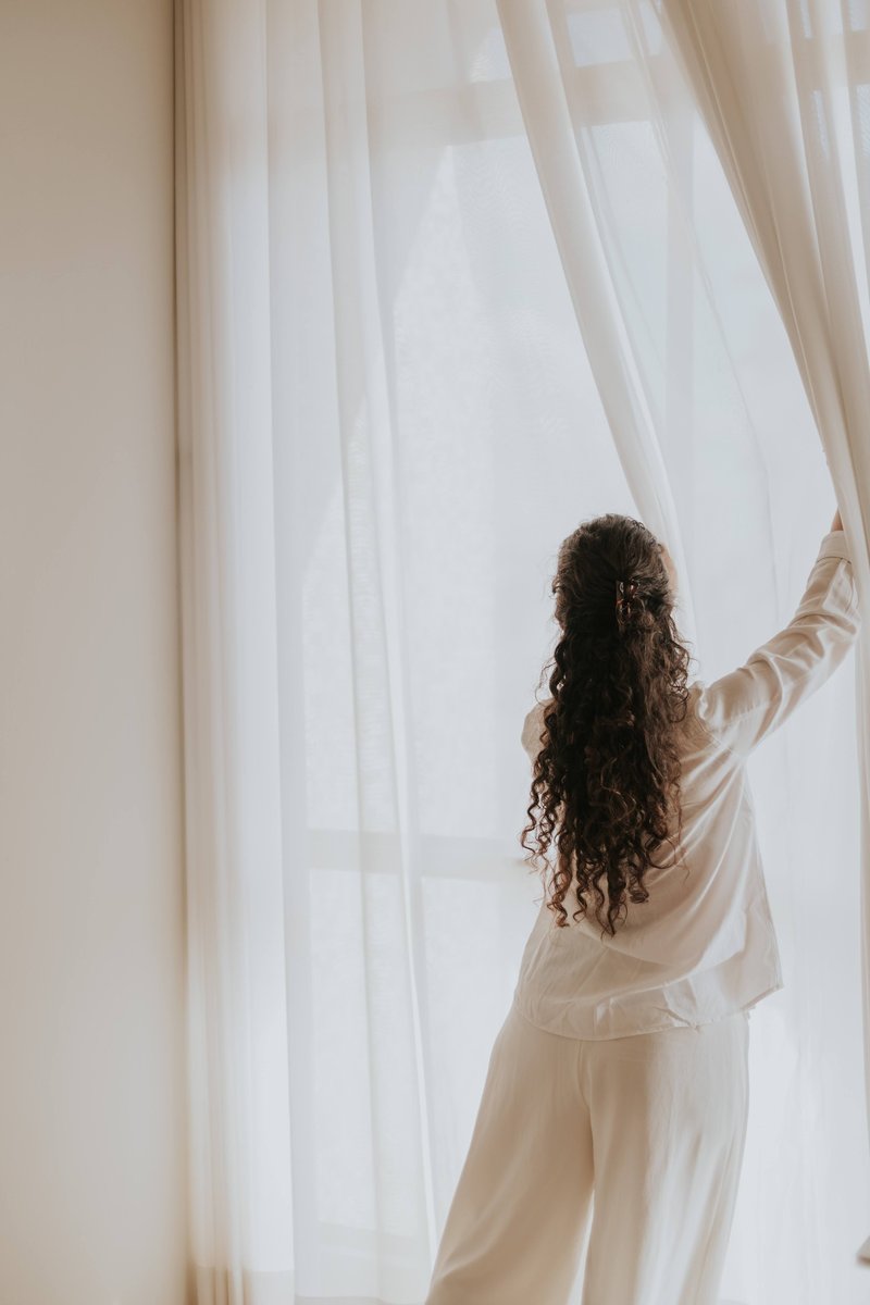 Woman seen from behind opening the curtains of a bright window in a Montreal rental apartment.